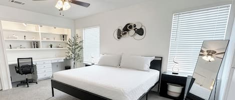 A bedroom with a bed, a desk, a chair, a wardrobe, a ceiling fan, and a wall-mounted mirror.