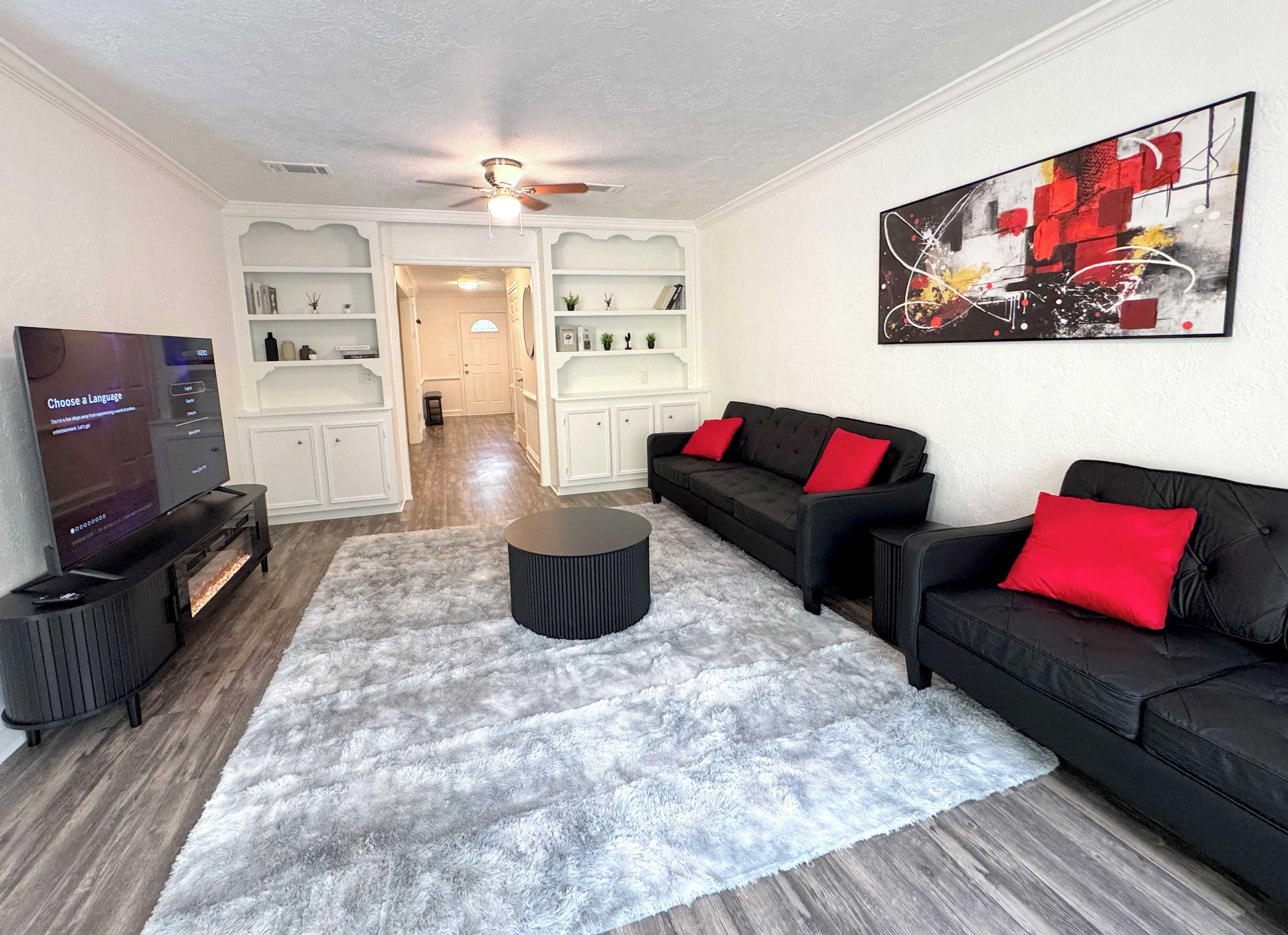 A living room with a black sofa set, a round coffee table, and a flat-screen TV.