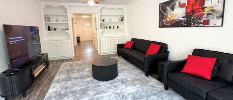 A living room with a black sofa set, a round coffee table, and a flat-screen TV.