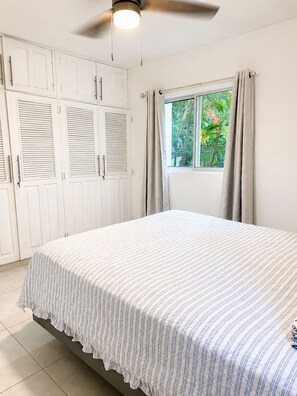 Ein Schlafzimmer mit einem Bett, einem Deckenventilator, einem Fenster mit Vorhängen und einem Kleiderschrank.