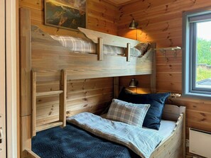 Un lit superposé avec une tête de lit, une fenêtre donnant sur un paysage verdoyant et une lampe fixée au mur.