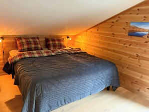A bedroom with a wooden sloped ceiling, a bed with plaid bedding, and a nightstand with a lamp.