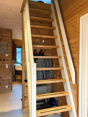 A wooden staircase leading to a lower level with a view of a room with a bed and a window.