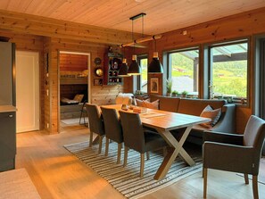 Un intérieur de chalet chaleureux avec un coin repas, des sièges et une vue sur l’extérieur.