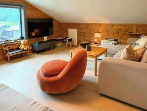 A cozy living room with a television, a sofa, a unique orange chair, and a wooden wall.