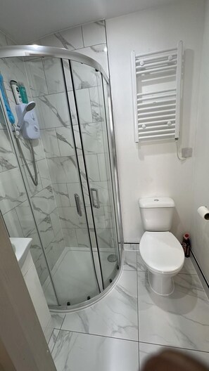 Un baño con ducha envuelta en vidrio, inodoro y perchero para toallas.
