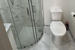 A bathroom with a glass-enclosed shower, a white toilet, and a white sink. - Studio Sleeps 2 With Wifi (Thornton Heath)