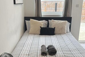 Una cama con ropa de cama a rayas y varias almohadas, una ventana con cortinas y vista a una cerca de madera.