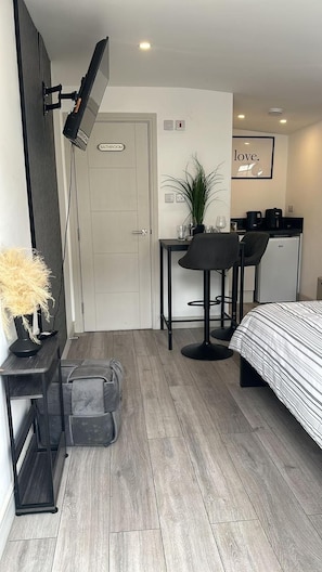 Habitación de hotel pequeña con cama, escritorio, silla, kitchenette y baño.