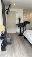 Habitación de hotel pequeña con cama, escritorio, silla, kitchenette y baño.