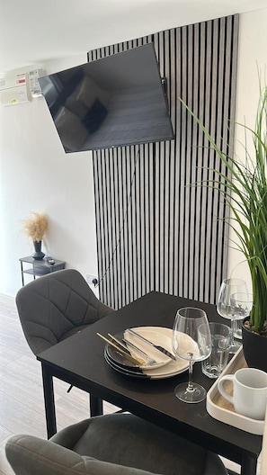 Un comedor con una mesa dispuesta para dos personas, un televisor montado en la pared y una planta en maceta.