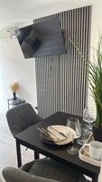 Un comedor con una mesa dispuesta para dos personas, un televisor montado en la pared y una planta en maceta.