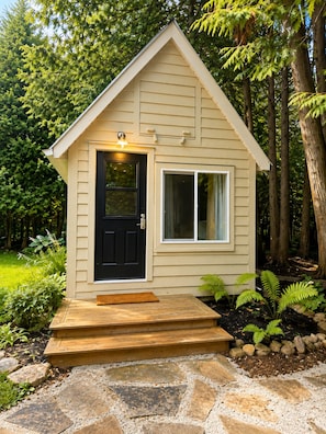 A small, single-story wooden cabin with a black front door and a window to the right.