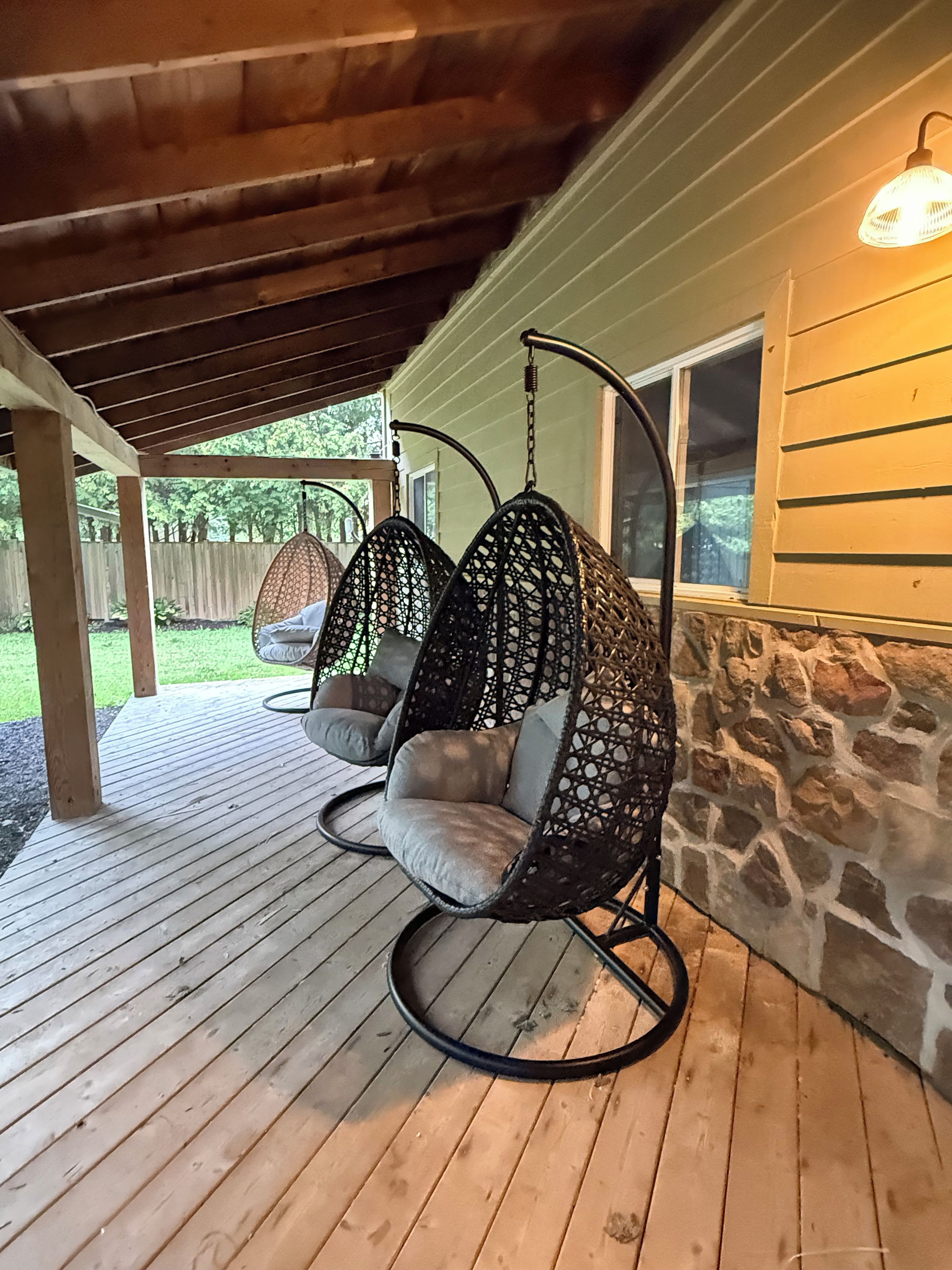 Une terrasse en bois avec un fauteuil suspendu et un mur en pierre.