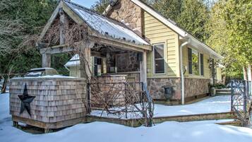 A two-story house with a stone foundation, a covered porch, and a snow-covered roof.
