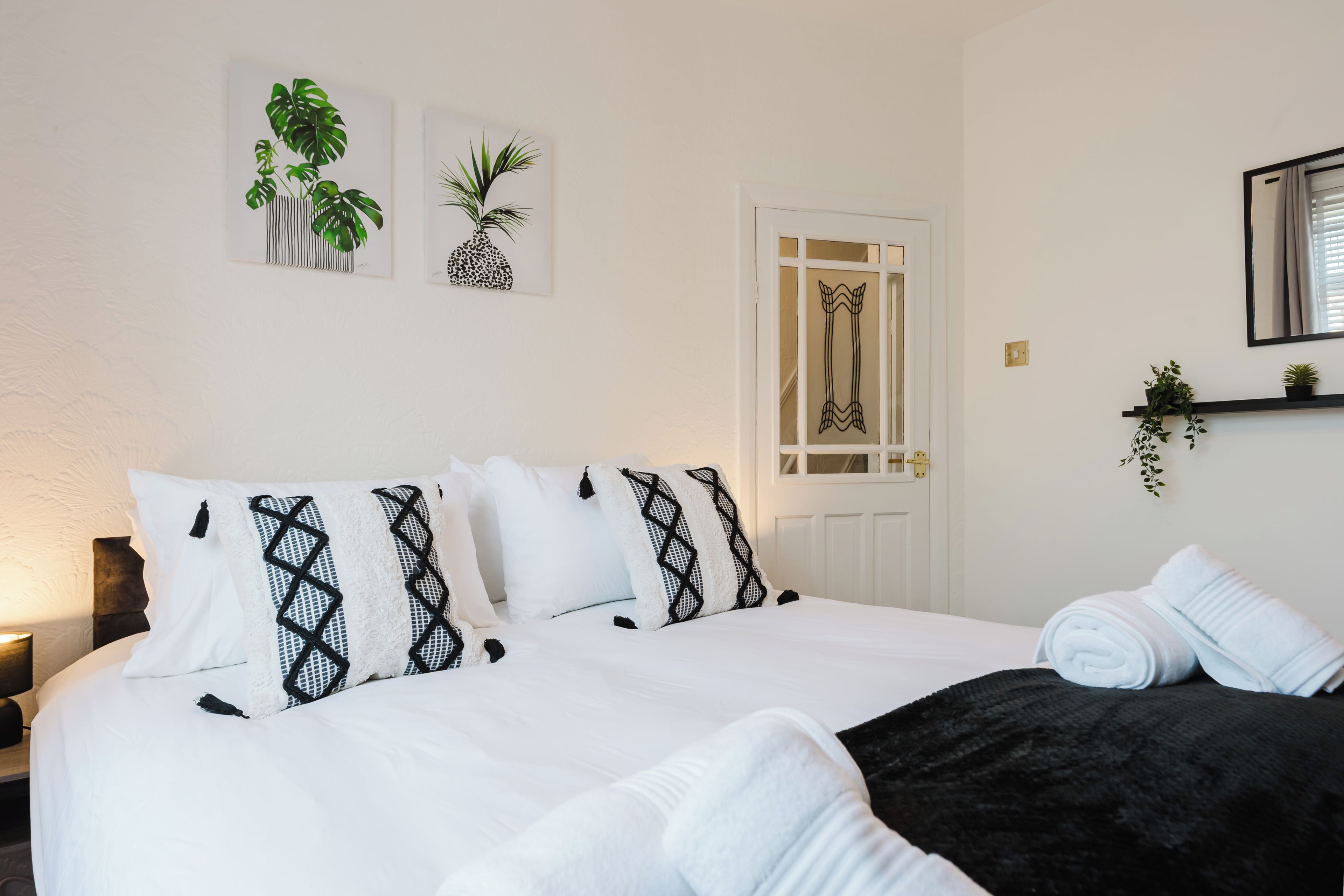 Habitació d'hotel amb llit, almoinos, una taula de nit, làmpada, porta i obra d'art a la paret.