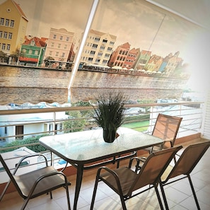 Een eetgedeelte met een tafel en stoelen, met uitzicht op een rivier en gebouwen op de achtergrond.