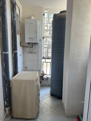 Ein Zimmer mit einem weißen Warmwasserbereiter, einem großen Wassertank und einem bedeckten Gegenstand auf dem Boden.