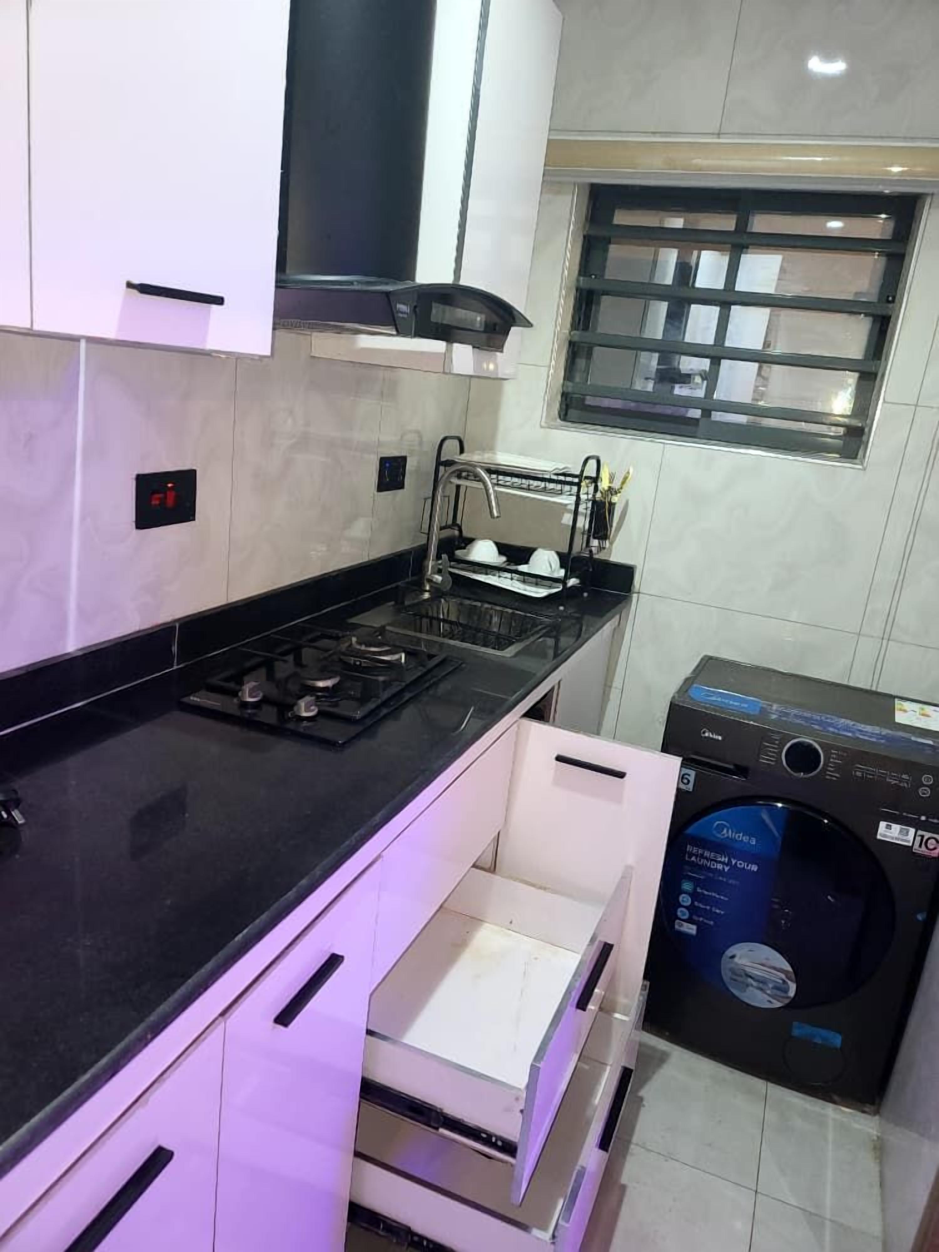 A compact kitchen with a gas stove, a built-in oven, a washing machine, and a window with a grid pattern.