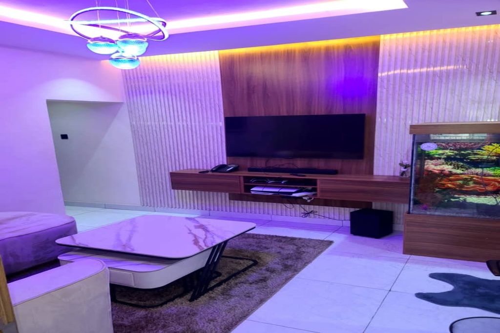 A modern living room with a flat-screen TV mounted on a wooden wall, a glass fish tank, and a sofa.
