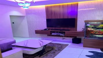 A modern living room with a flat-screen TV mounted on a wooden wall, a glass fish tank, and a sofa.