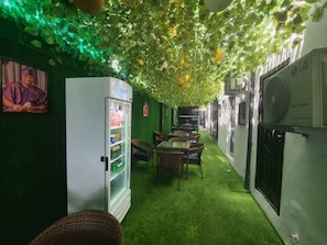 A corridor with artificial green foliage on the ceiling, a refrigerator stocked with beverages, and a wall-mounted air conditioning unit. - Dual Hotel and Apartments Limited (Lagos)