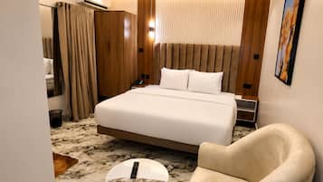 Une chambre d’hôtel avec un grand lit, un coin salon comprenant un fauteuil, une petite table ronde et un luminaire au plafond.