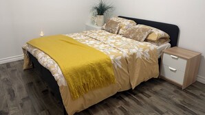 A neatly made bed with a yellow throw blanket, a bedside table with a lamp, and a small potted plant on the nightstand. - Perfect basement apartment in Milton (Milton)
