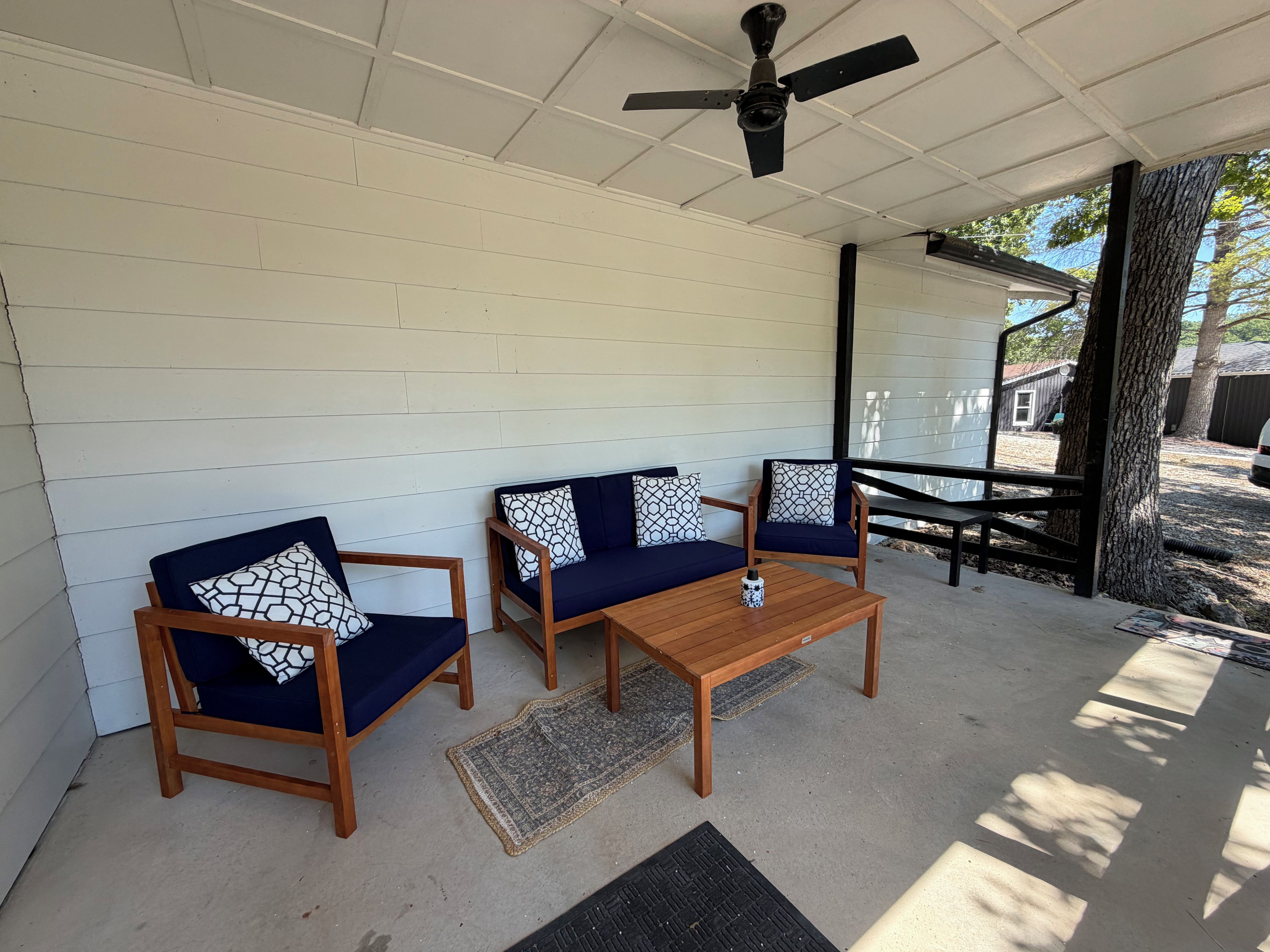 A covered patio with two wooden chairs and a table, a ceiling fan, and a view of a backyard.