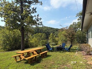 A picnic area with a wooden table and benches, surrounded by trees and a grassy lawn.