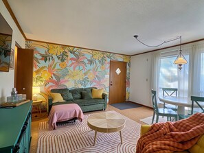 A living room with a sofa, a coffee table, a patterned rug, and a tropical wallpaper.
