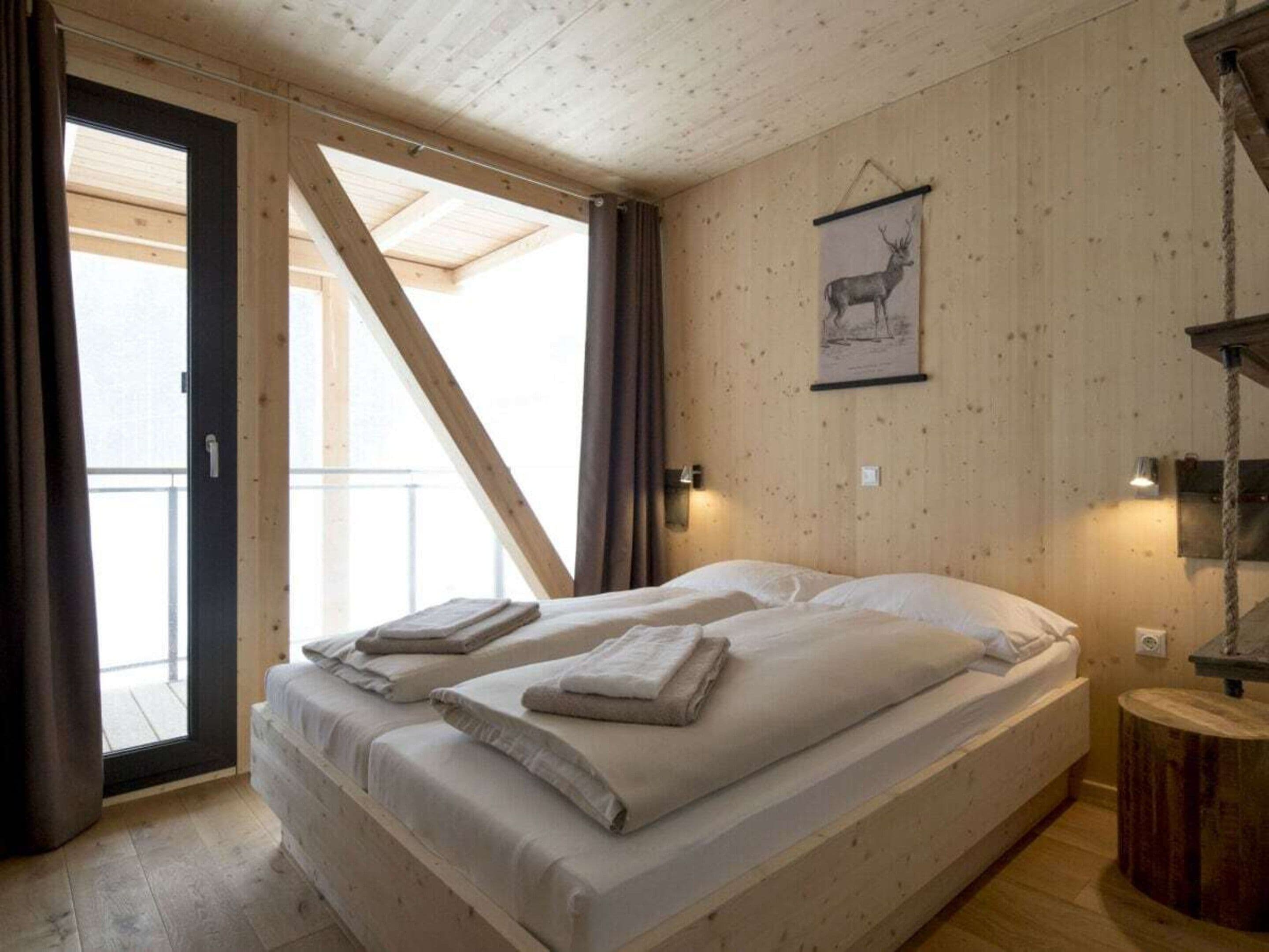 Ein Zimmer mit einem Bett, Holzboden, einem gerahmten Bild an der Wand und einem fenster mit Vorhängen.