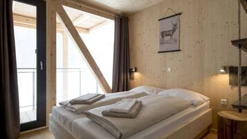 Ein Zimmer mit einem Bett, Holzboden, einem gerahmten Bild an der Wand und einem fenster mit Vorhängen.