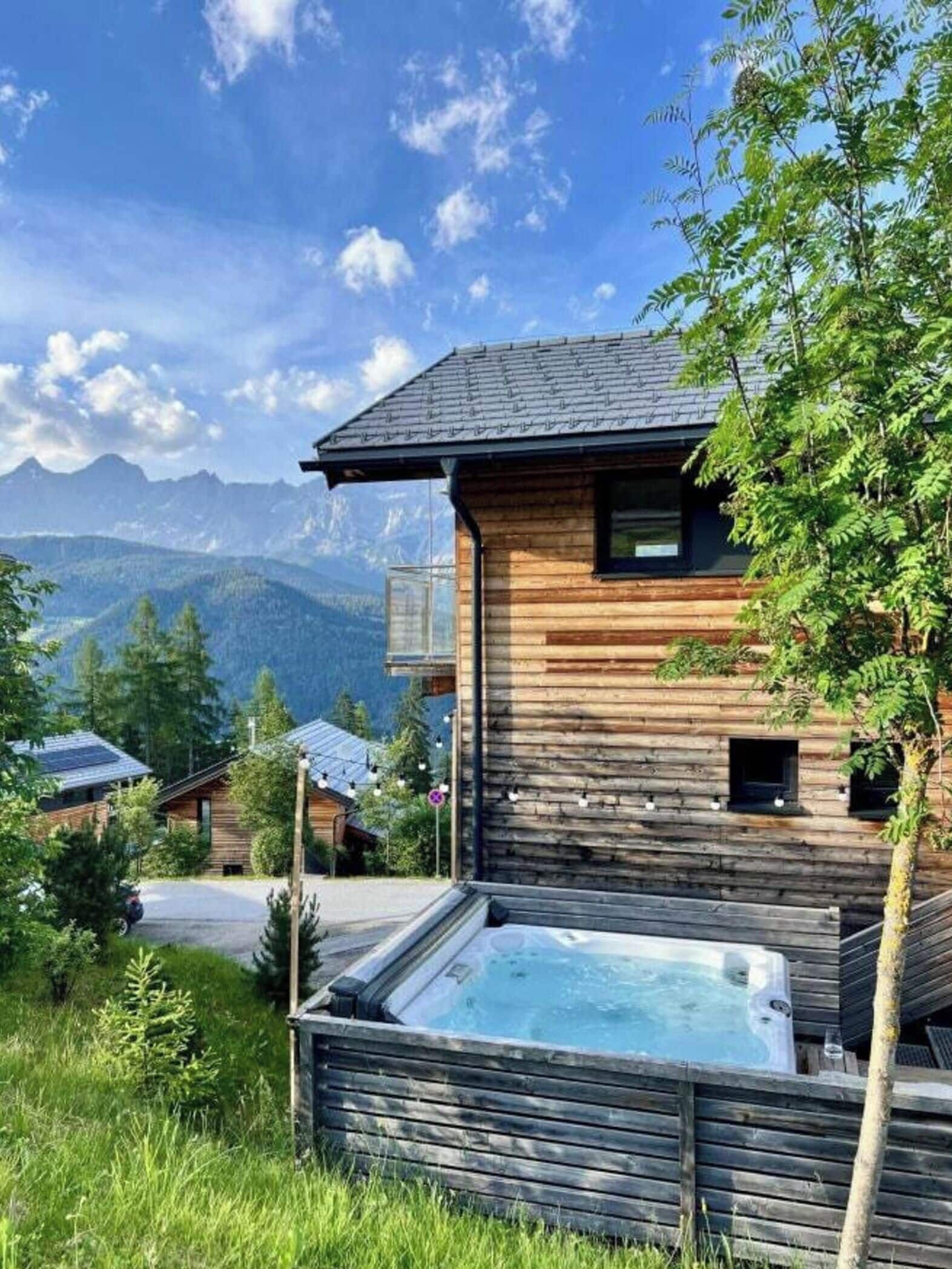 Eine Holzhütte mit Whirlpool, umgeben von Bergen und Grün.