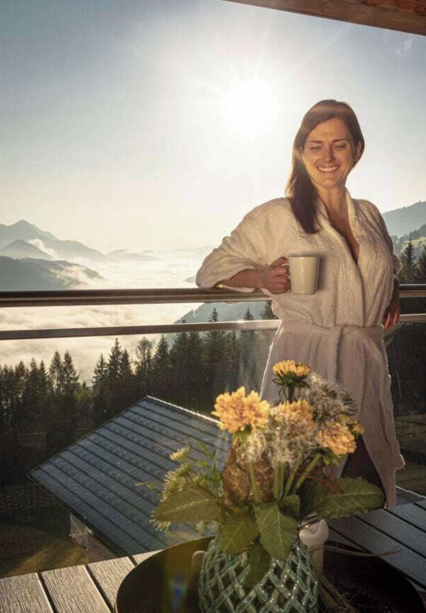 Une personne vêtue d’une robe, sur un balcon, avec vue sur les montagnes et les nuages.