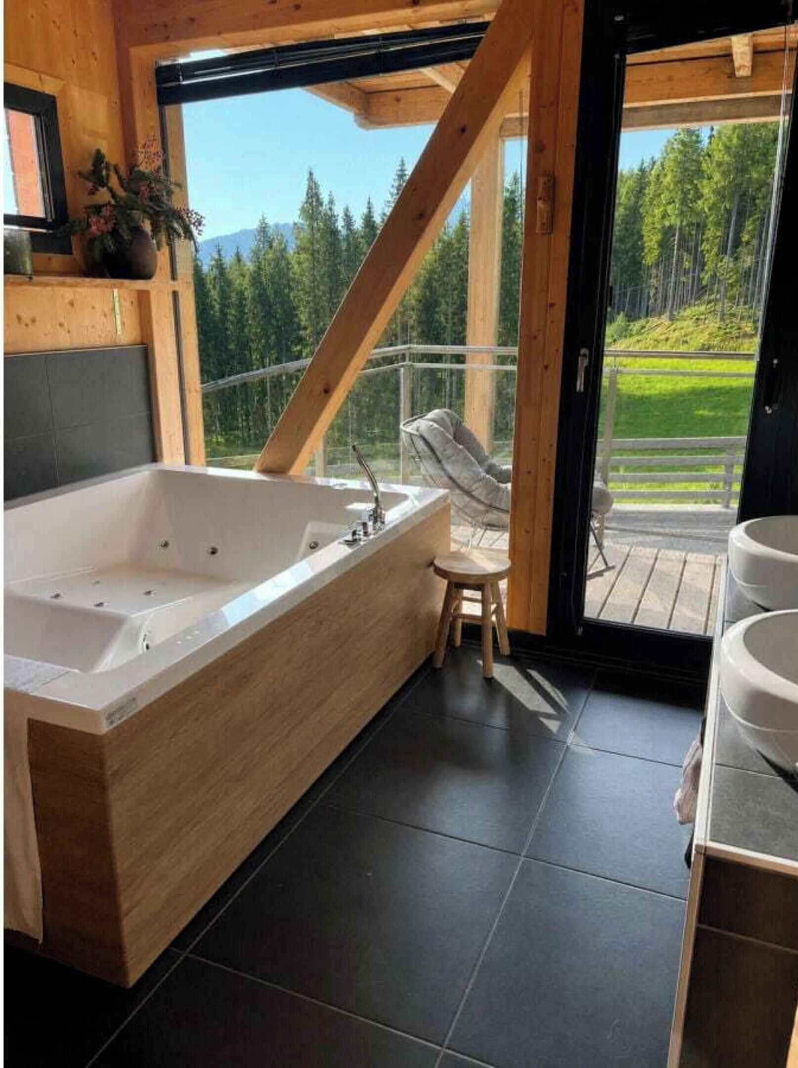 Un baño moderno con una bañera grande, una ventana con marco de madera y vistas a un bosque.