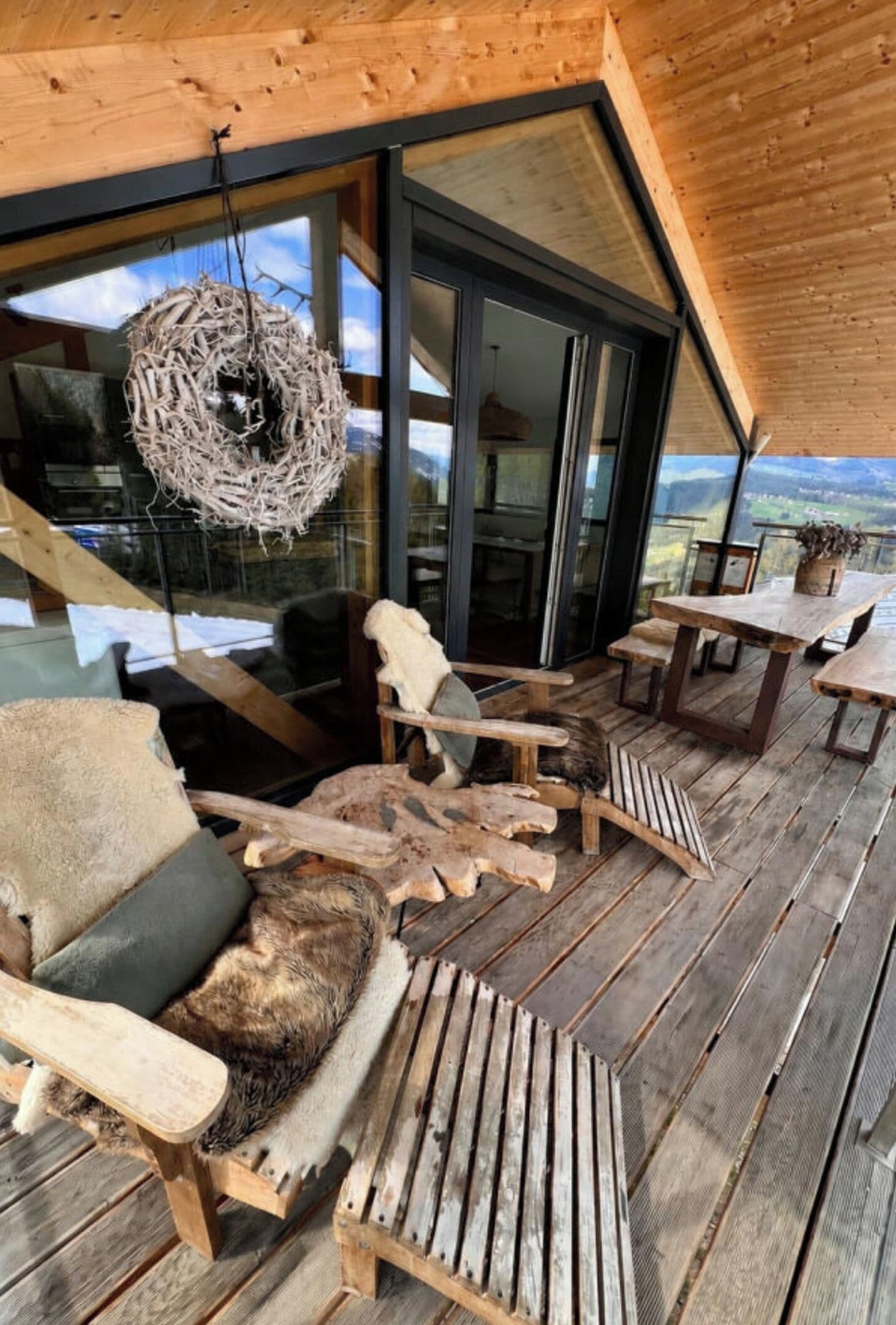 A wooden deck with outdoor seating, a hanging wreath, and a view of the landscape.