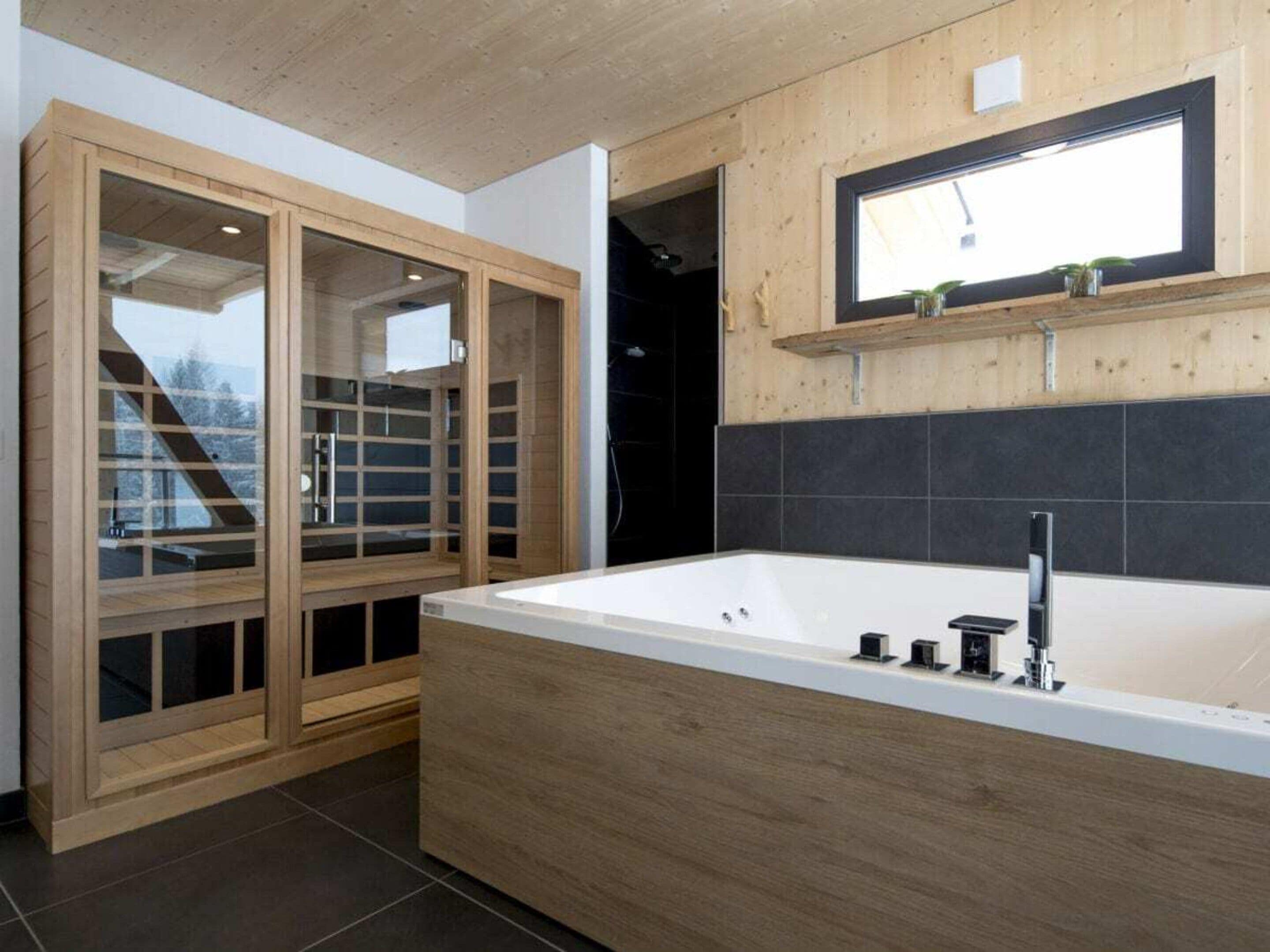 A modern bathroom with a freestanding bathtub, wooden cabinetry, and a window above the sink.