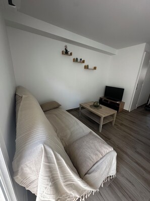 Un salon comprenant un canapé, une table basse, un téléviseur à écran plat et des étagères murales ornées d’objets décoratifs.