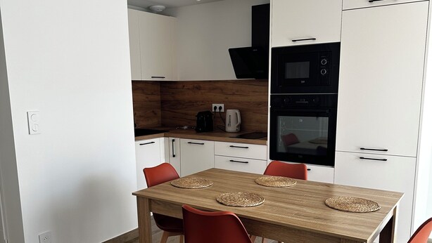 Ett modernt kök med vita skåp, ett matbord i trä och röda stolar.