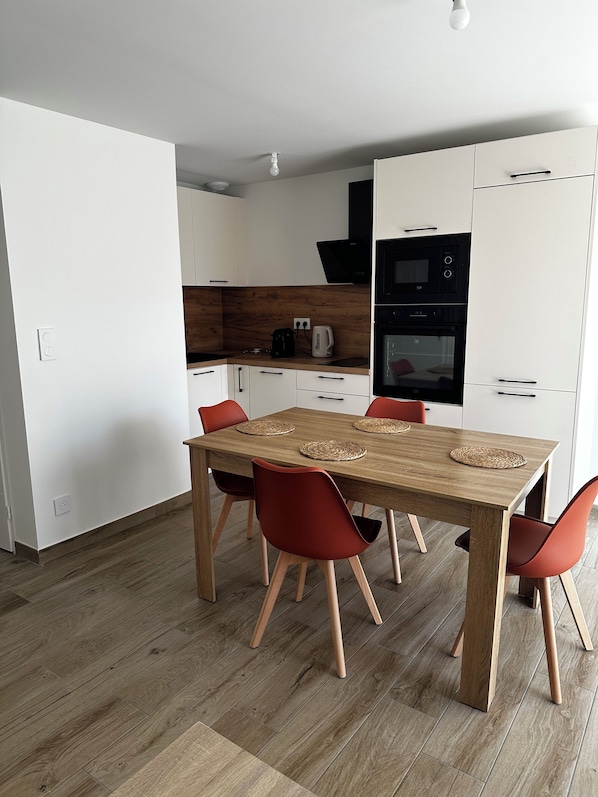 Une cuisine moderne avec des meubles blancs, une table à manger en bois et des chaises rouges.