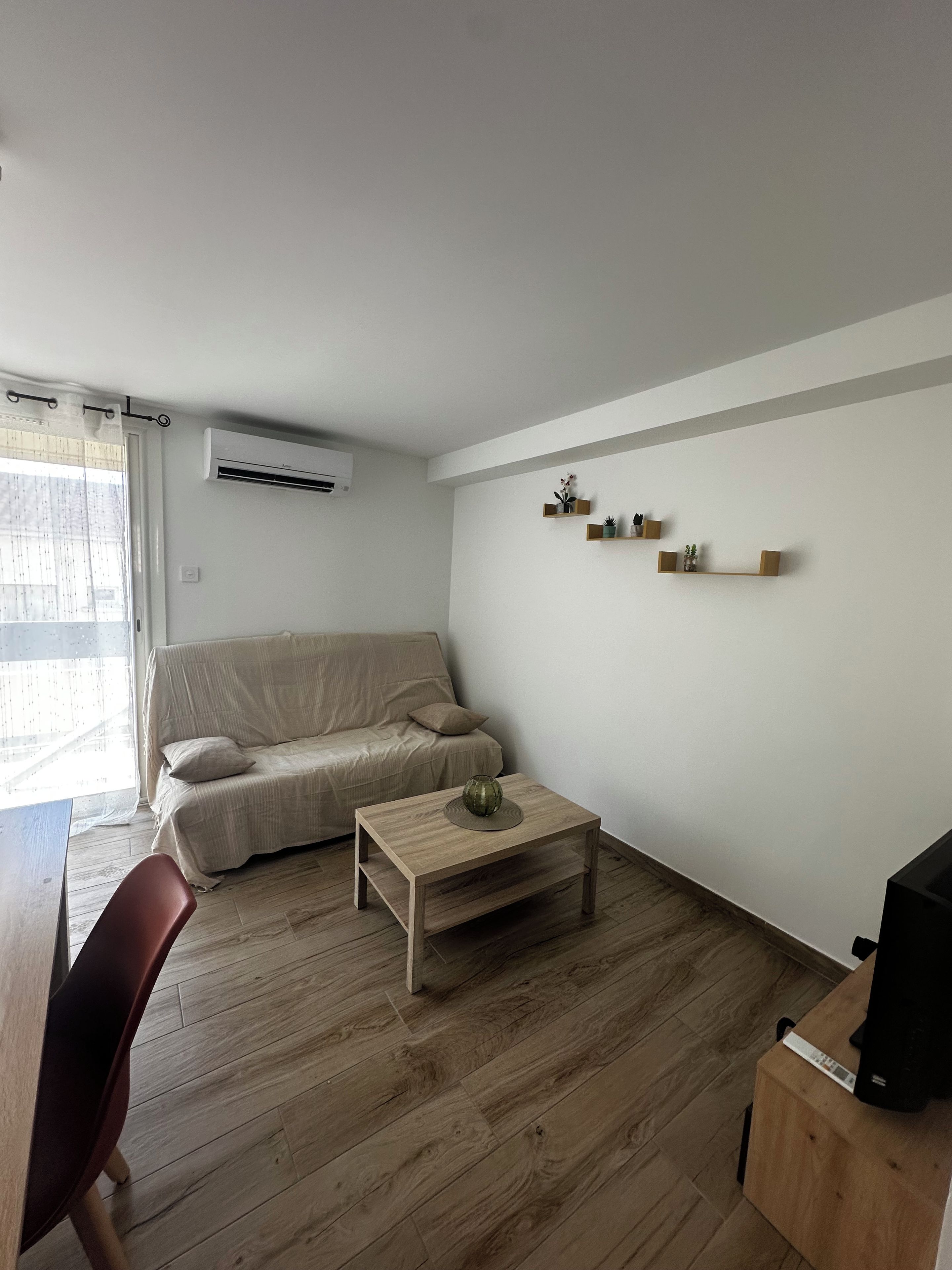 Ein Wohnzimmer mit einer Couch, einem Couchtisch, einer TV-Konsole und einem an der Wand befestigten Regal mit Dekoration.
