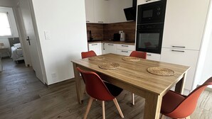 Ett modernt kök med vita skåp, ett matbord i trä och röda stolar.