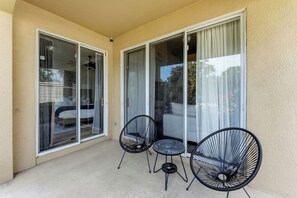 A balcony with a sliding glass door, two black wireframe chairs, and a small round table. - Spacious 3 BR with Pool - Near St. Pete Beaches, Downtown & Tampa (Pinellas Park)
