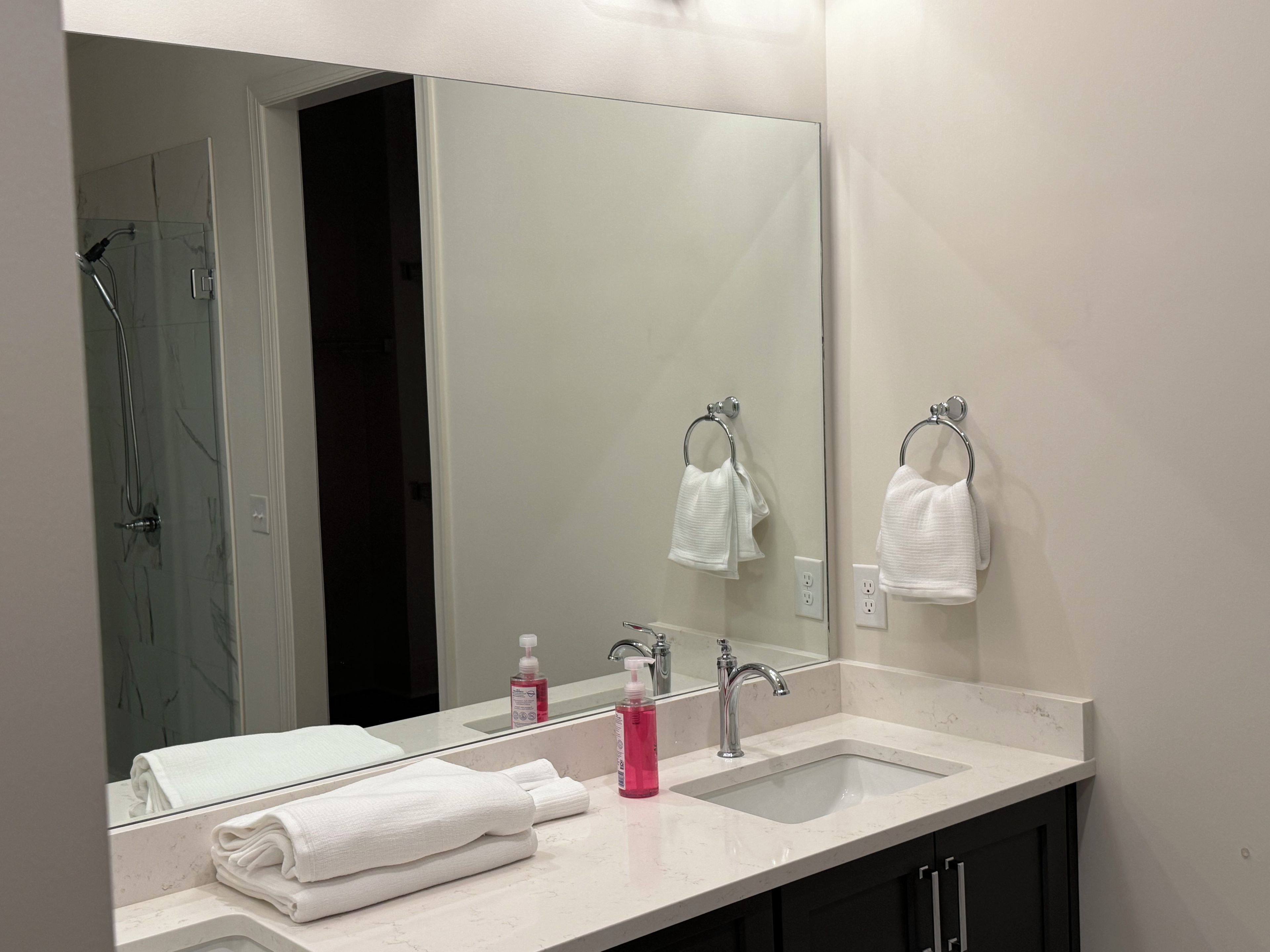 Ein modernes Badezimmer mit einem großen Spiegel, zwei Waschbecken und einer Dusche.