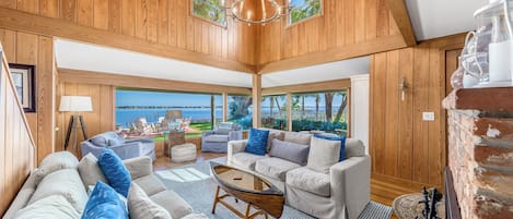 A spacious living room with a large view of the sea, wooden walls, and a chandelier.
