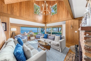 A spacious living room with a large view of the sea, wooden walls, and a chandelier.