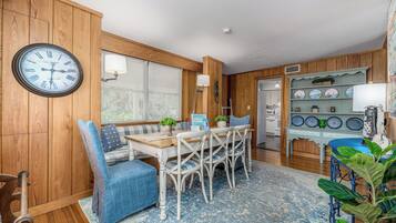 A cozy kitchen with wooden walls, a round clock, a dining table with chairs, and a shelf with plates.