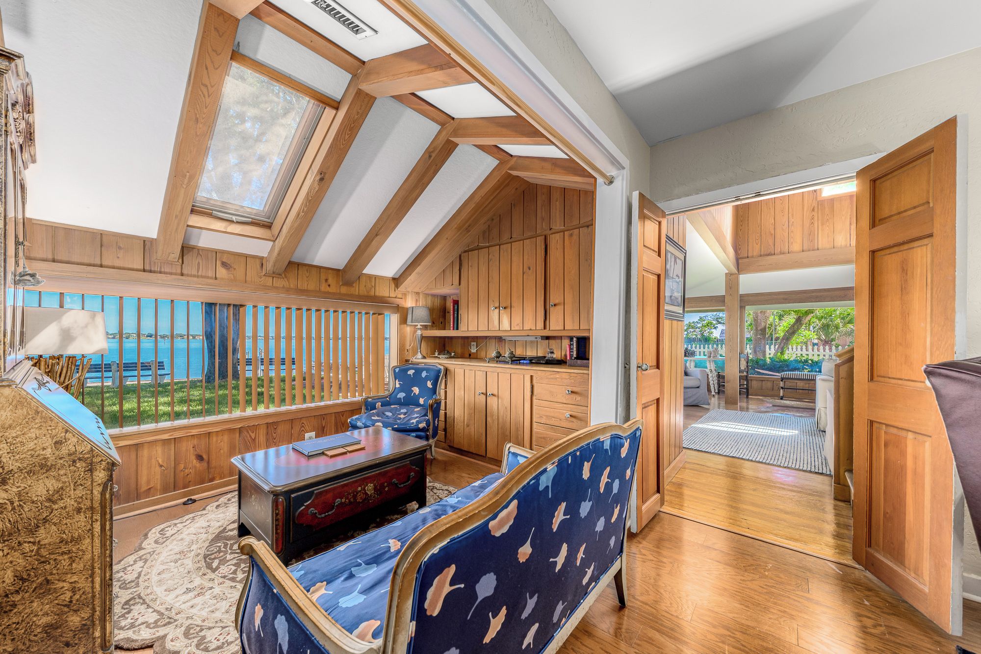 Una habitación con vigas de madera, vista al mar, un sofá de tapiz azulado y un aparador de madera.