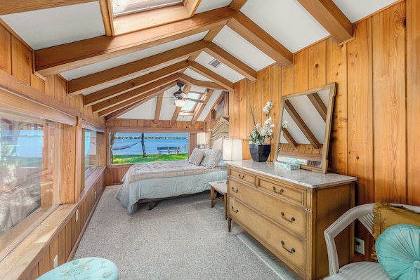 A bedroom with a bed, dresser, and a large mirror. There is a window with a view of a body of water and a dock.